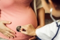 Doctor using stethoscope to examine a pregnant woman's belly.