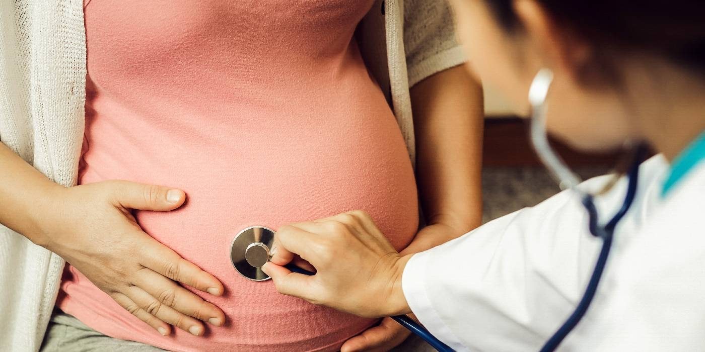 Doctor using stethoscope to examine a pregnant woman's belly.